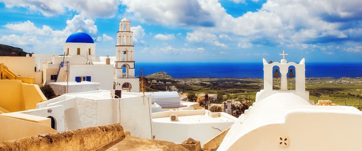 A coastal town with white buildings, a blue dome, and a bell tower.