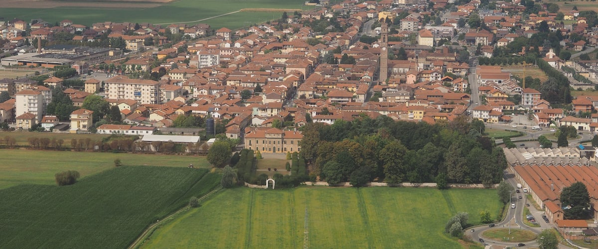 A densely built urban area with a mix of residential and commercial buildings, surrounded by green fields and a prominent church tower.