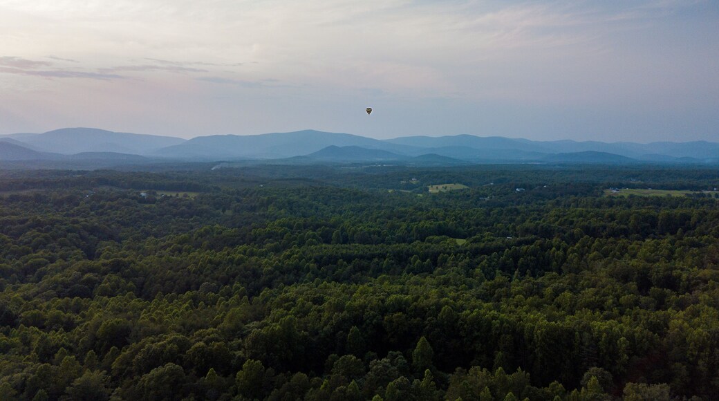 A hot air balloon sails in the distance over the Virginia countryside with blue ridge mountains in the background. Horizontal landscape oriented photo taken in Albemarle county, Ruckersville, Virginia