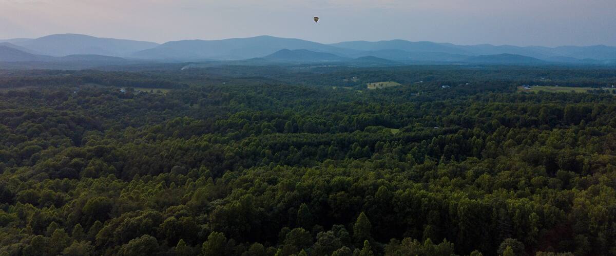 A hot air balloon sails in the distance over the Virginia countryside with blue ridge mountains in the background. Horizontal landscape oriented photo taken in Albemarle county, Ruckersville, Virginia
