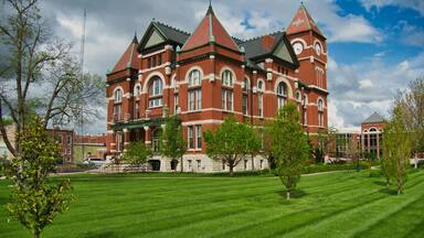 A large red brick building with a clock tower, surrounded by a well-maintained lawn and trees.