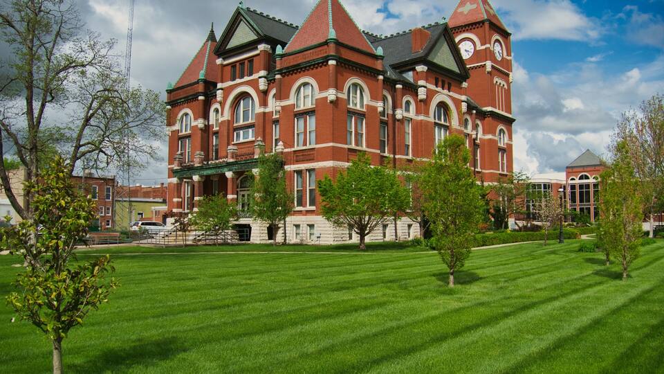 A large red brick building with a clock tower, surrounded by a well-maintained lawn and trees.