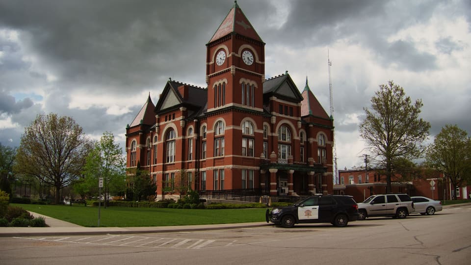 A large brick building with a clock tower, surrounded by trees and parked cars.