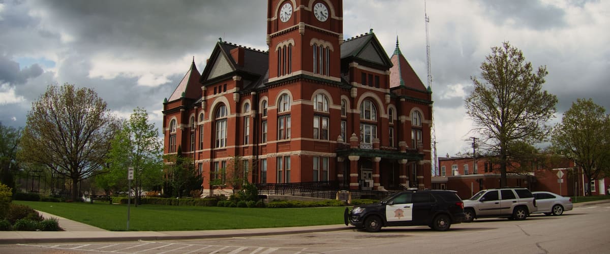 A large brick building with a clock tower, surrounded by trees and parked cars.