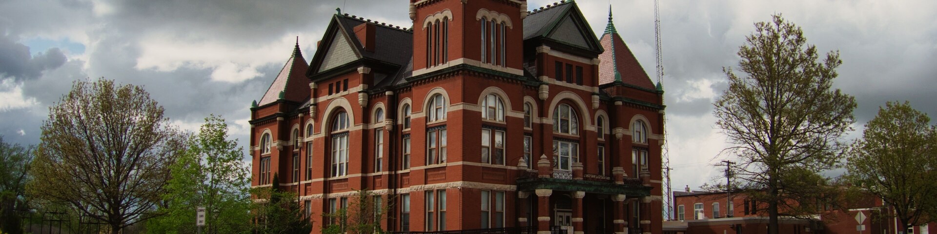 A large brick building with a clock tower, surrounded by trees and parked cars.