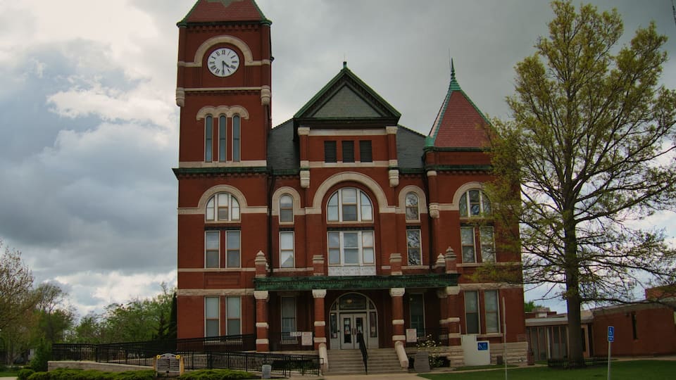 A large, historic red brick building with a clock tower and a green roof.