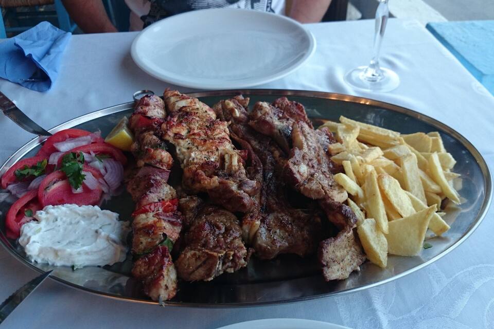 A plate of grilled meat, fries, and a side salad with tomatoes and onions.