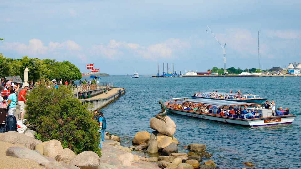A boat tour with passengers, a pier with people, and industrial structures in the background.