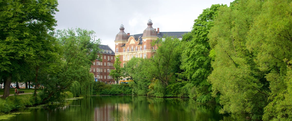 A serene lake with lily pads, surrounded by lush greenery and a historic building with domed towers in the background.
