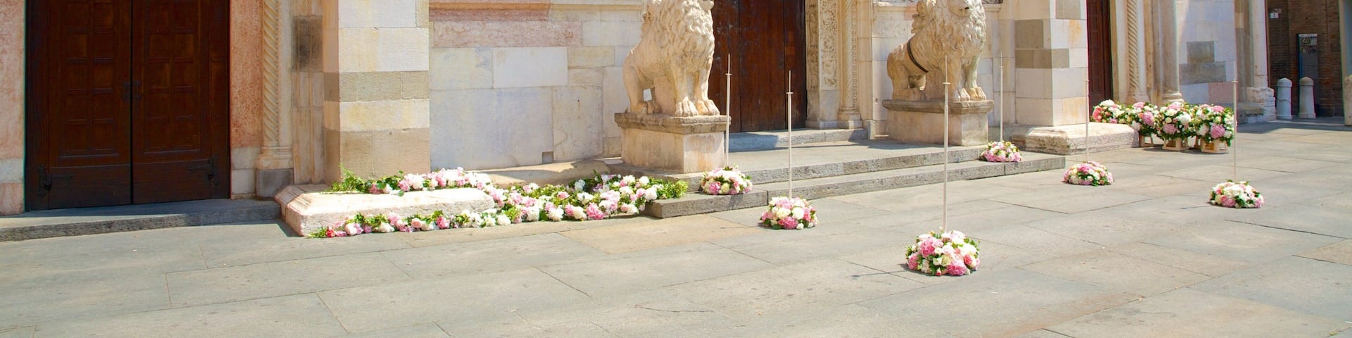 A historic building with ornate stone carvings, two lion statues, and a series of flower arrangements on the steps.