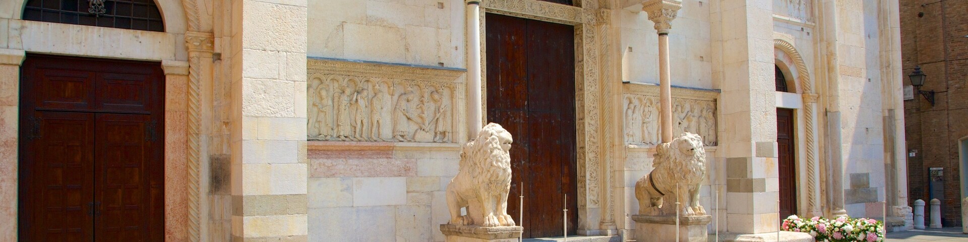 Un bâtiment historique orné de sculptures complexes en pierre, flanqué de deux statues de lions et agrémenté de plusieurs compositions florales disposées sur les marches.