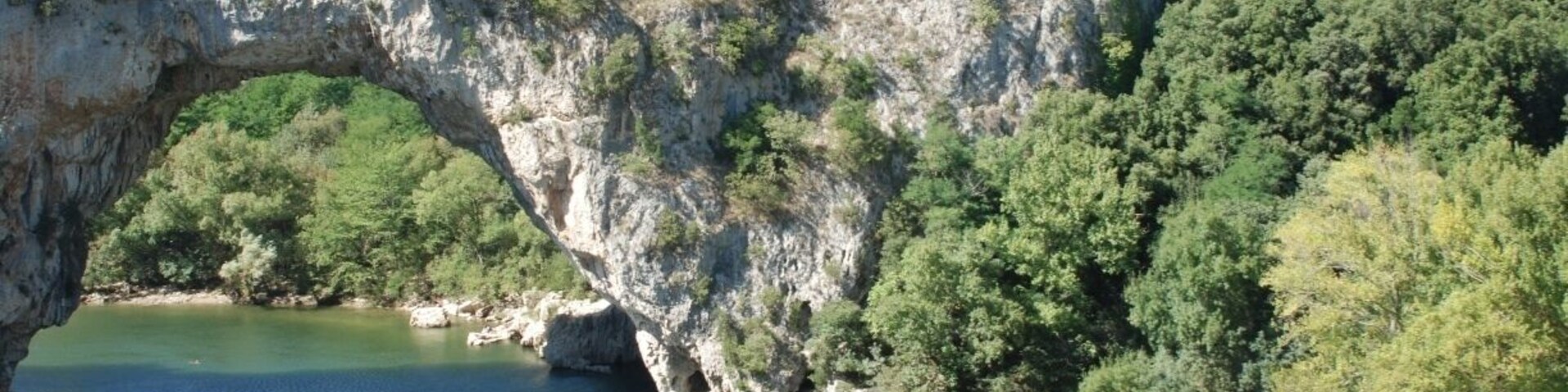Une arche naturelle enjambant une rivière, avec une plage et des arbres.