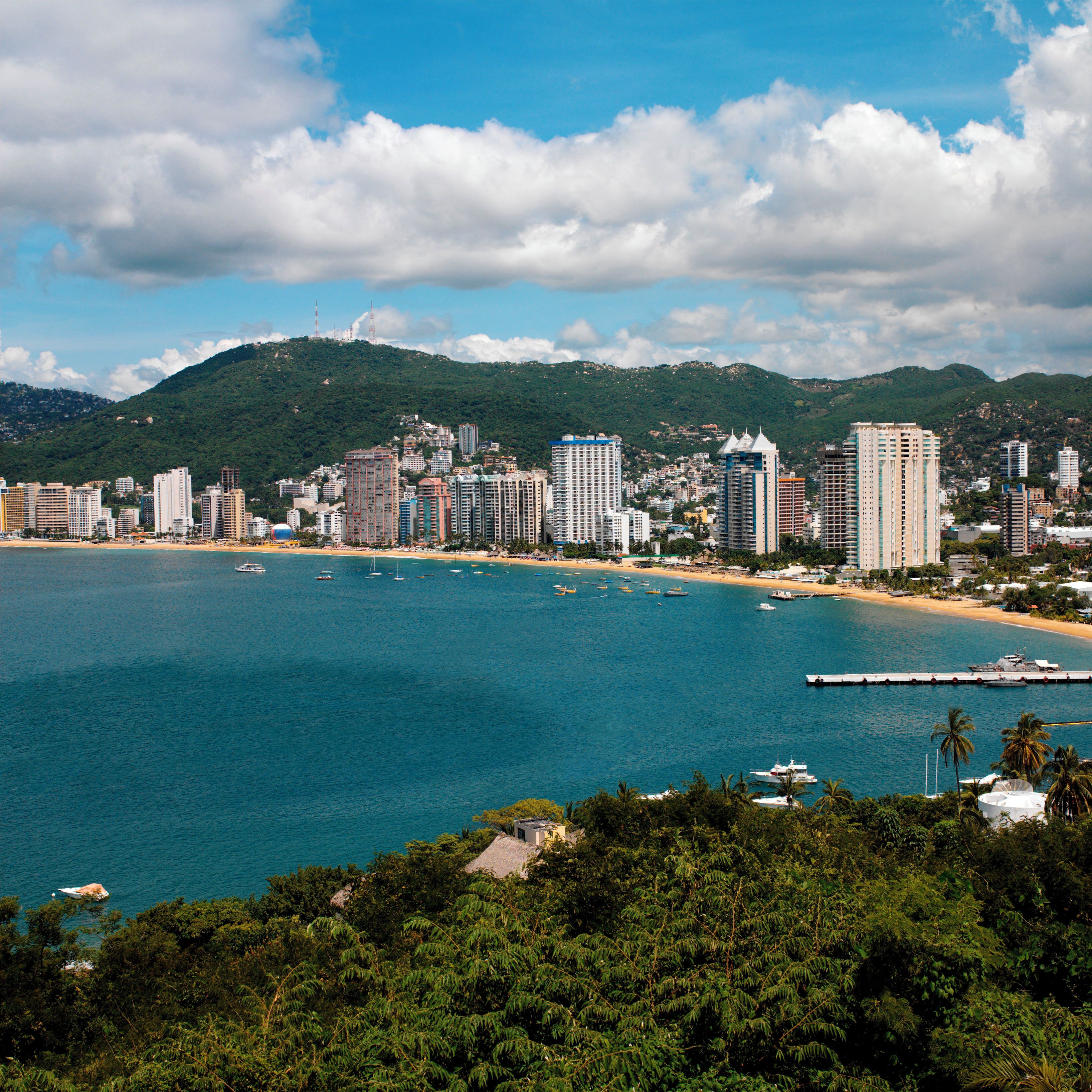 A coastal city with a beach, boats, and a mountainous backdrop.