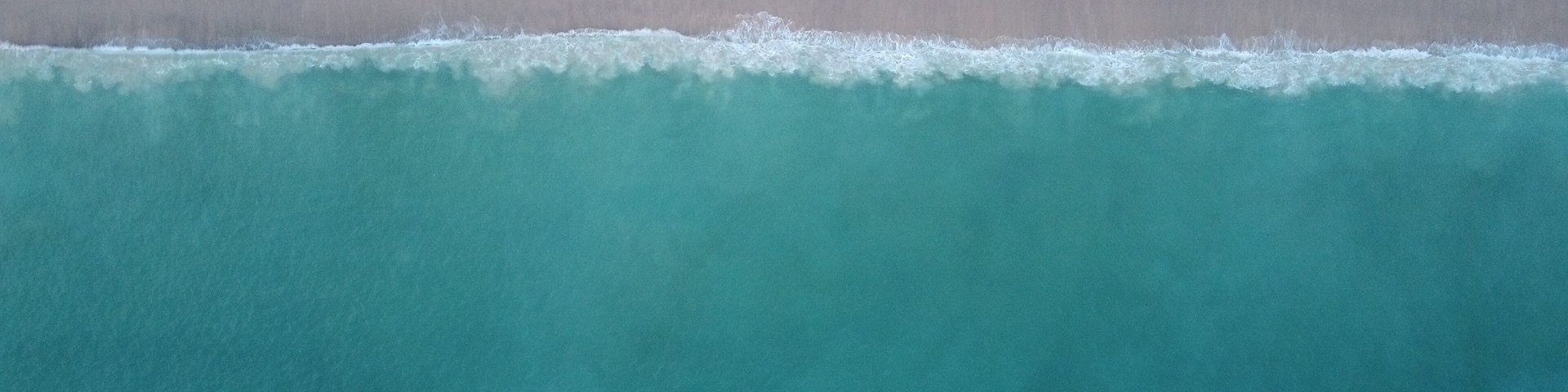 An aerial view of a beach with clear turquoise water, a sandy shore, and people scattered along the beach.