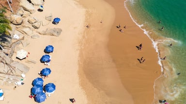 A sandy beach with large rocks, several blue umbrellas, and people swimming in the water.