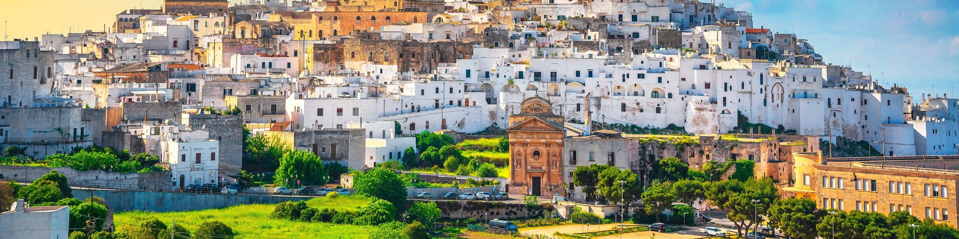 A historic cityscape with white buildings, a prominent church, and a hilltop fortress.