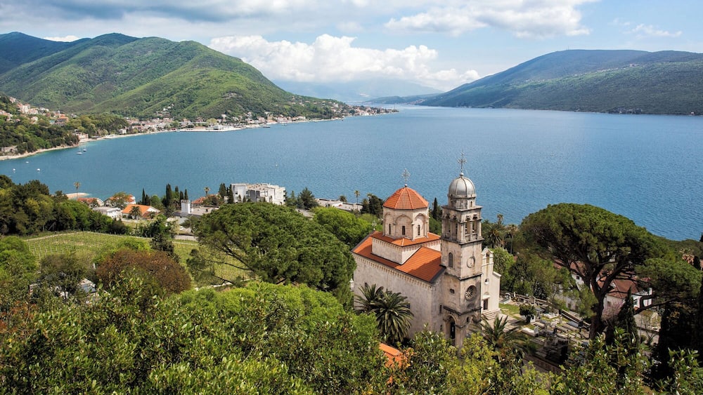 A coastal town with a prominent church, lush greenery, and a large body of water.