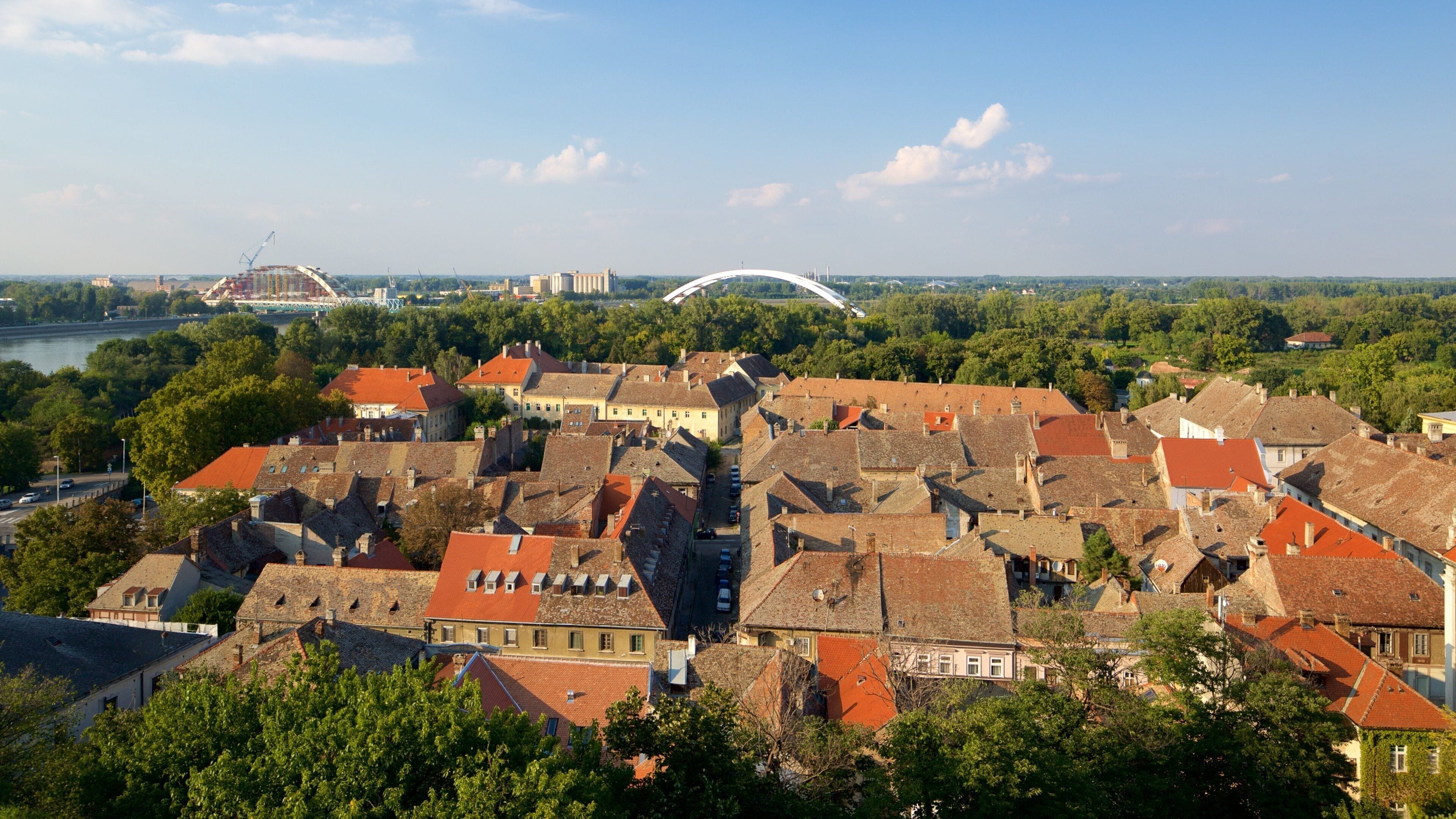 A historic town with red-roofed buildings, a river, and a bridge in the background.
