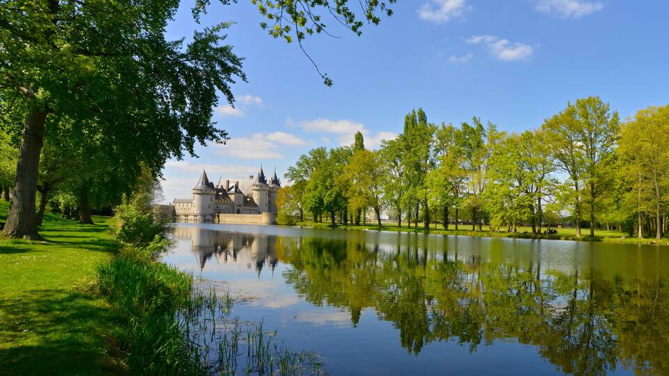 A castle by a calm river with lush greenery and clear skies.