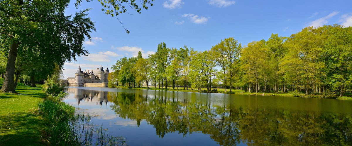 A castle by a calm river with lush greenery and clear skies.