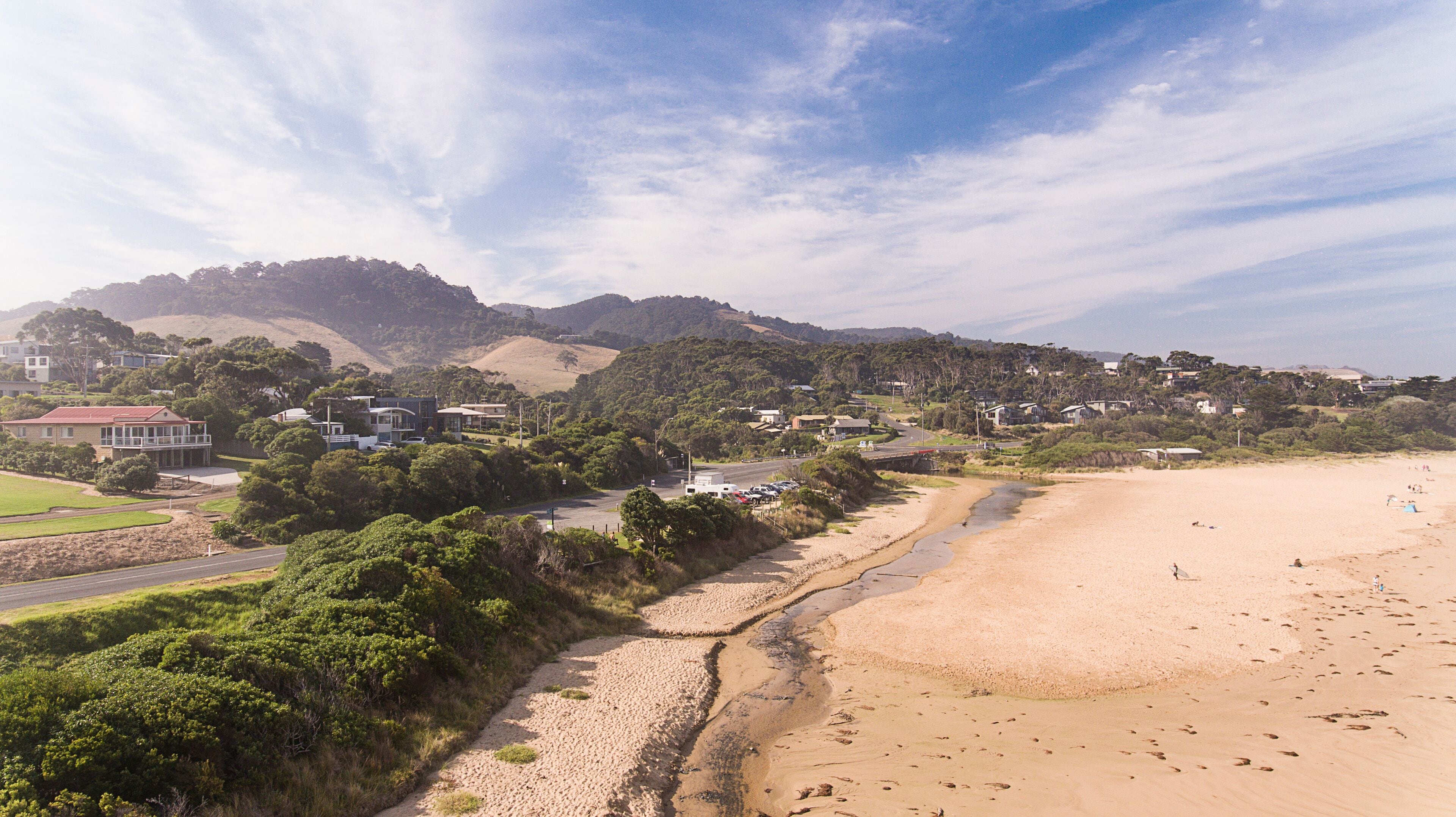 A coastal landscape with a sandy beach, a road, and residential buildings.