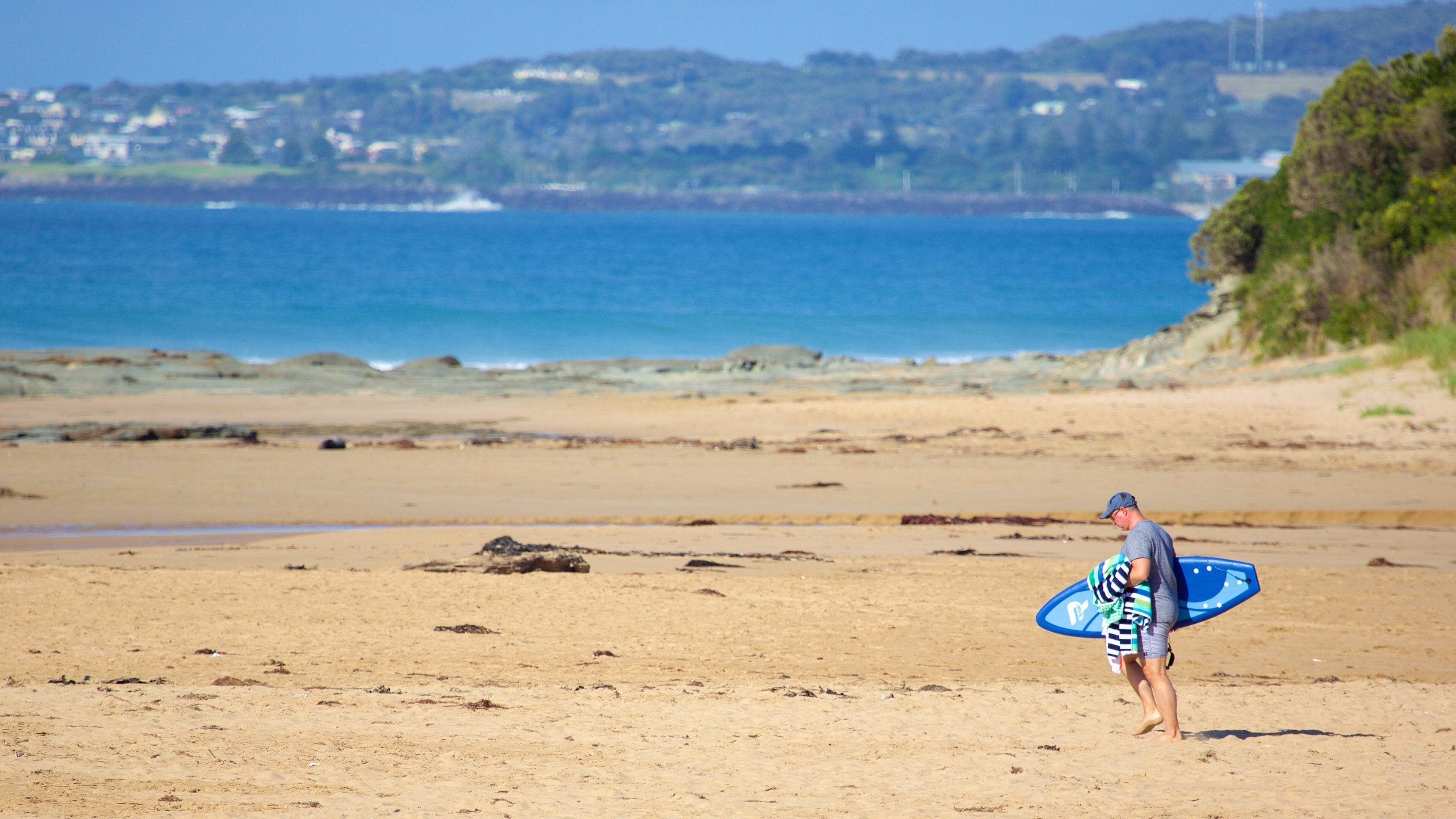 A beach with a person carrying a surfboard.