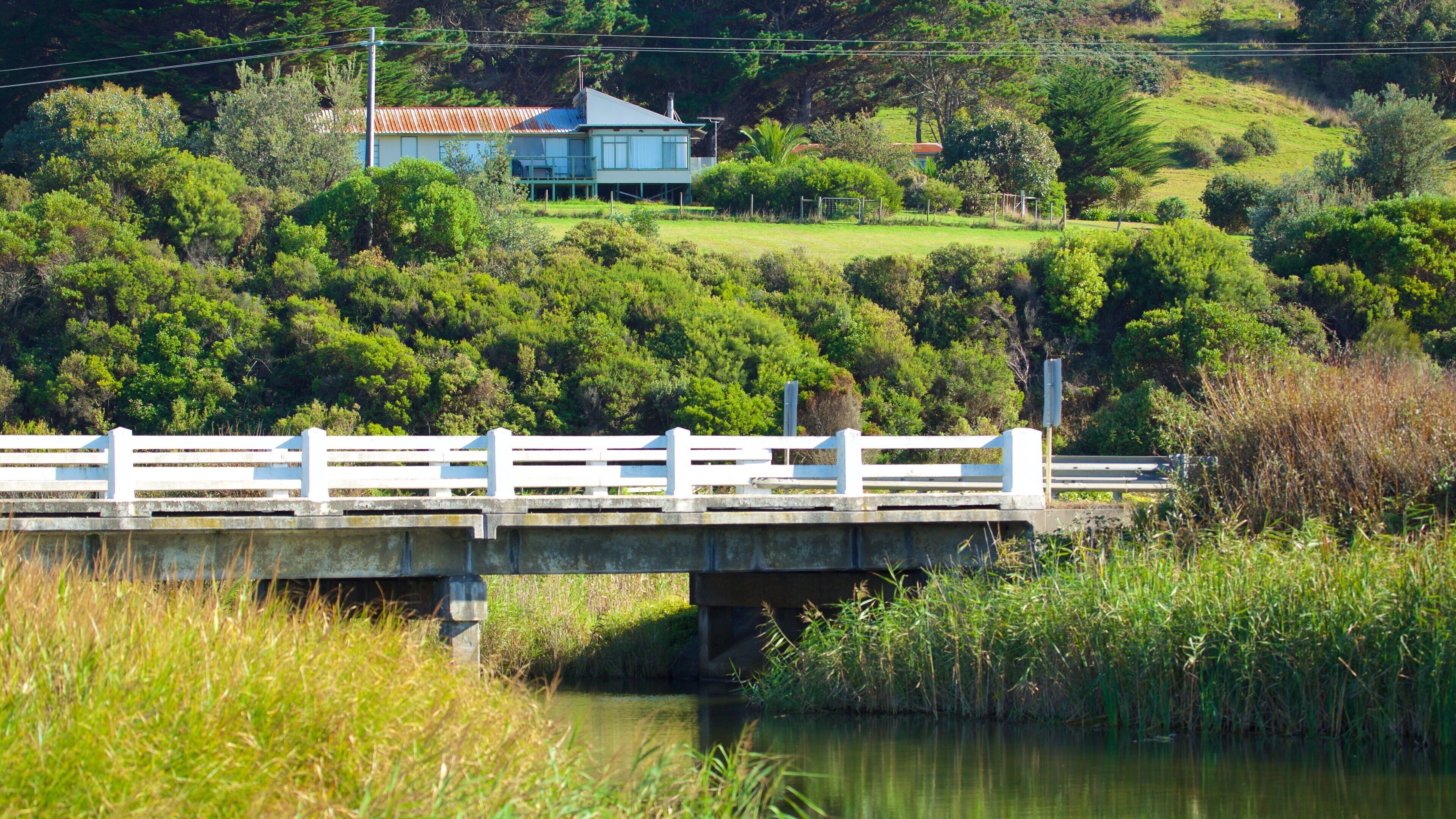 A bridge over a river with a house on a hill in the background.