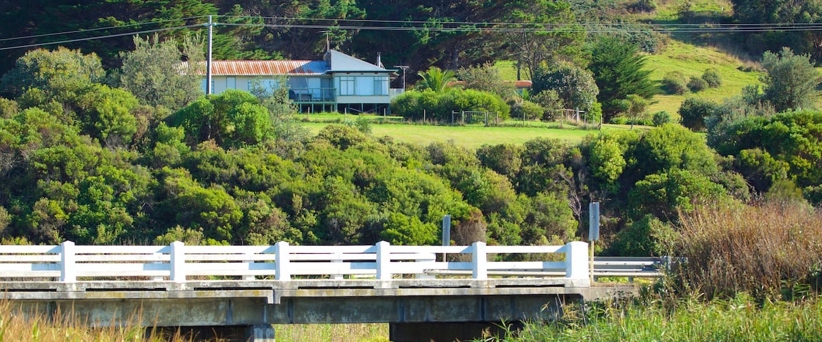 A bridge over a river with a house on a hill in the background.