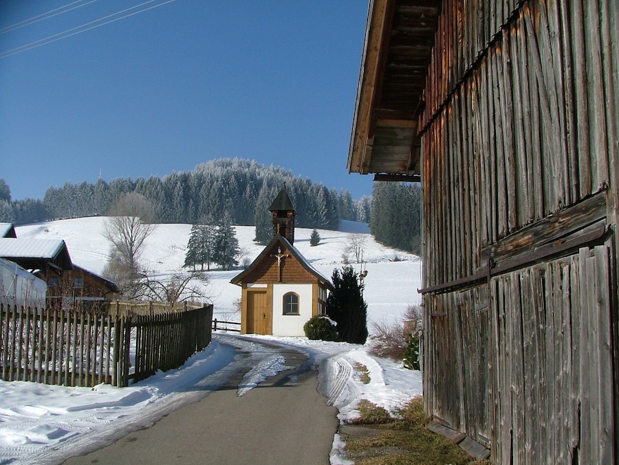 Un pueblo cubierto de nieve con una iglesia, edificios de madera y un cielo azul despejado.