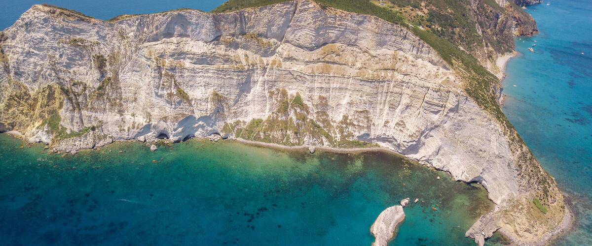 A coastal cliff with layered rock formations and a clear blue sea.