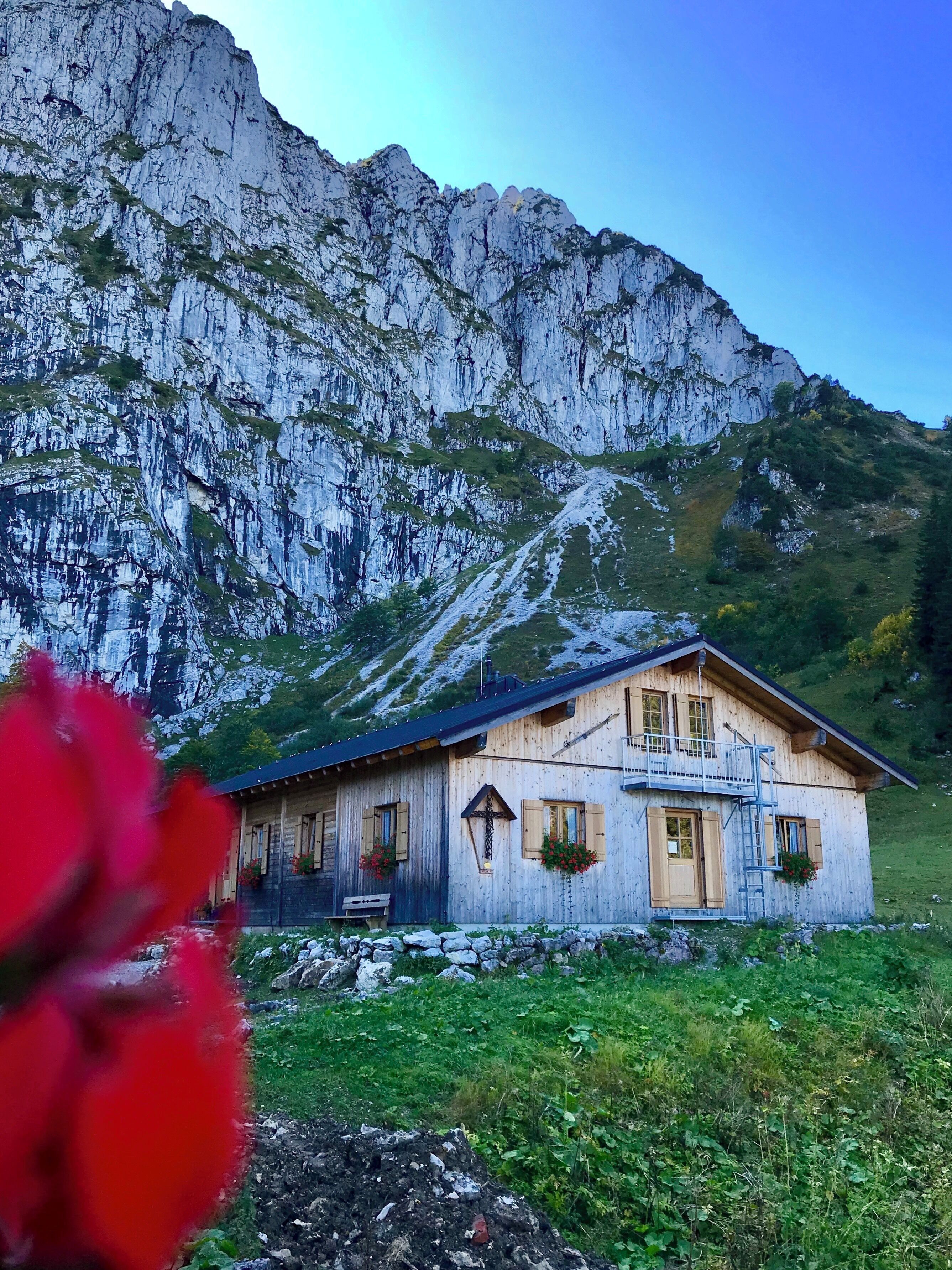 A wooden chalet with a balcony, set against a mountainous backdrop.