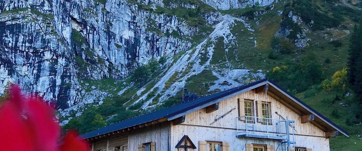 A wooden chalet with a balcony, set against a mountainous backdrop.