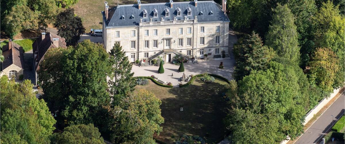 An aerial view of a large, historic stone building surrounded by lush greenery and a well-maintained garden.