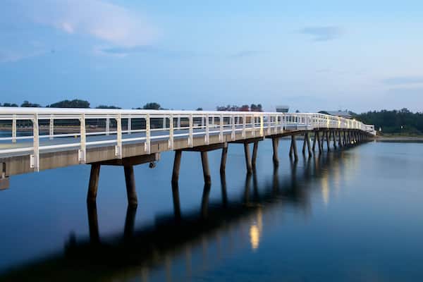 A long bridge over calm water with a clear sky.