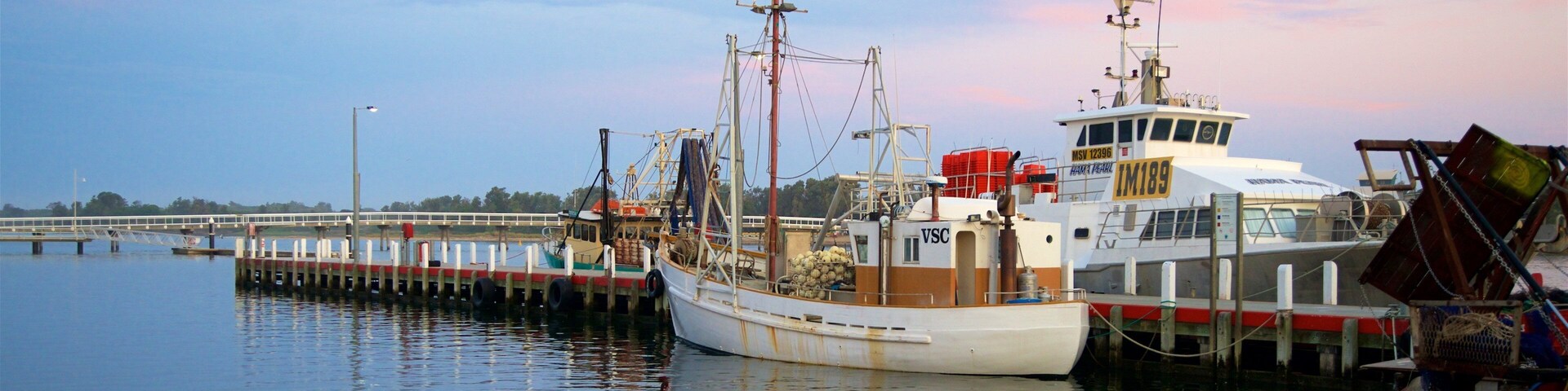 Un bote de pesca amarrado en un muelle, con un puente al fondo.