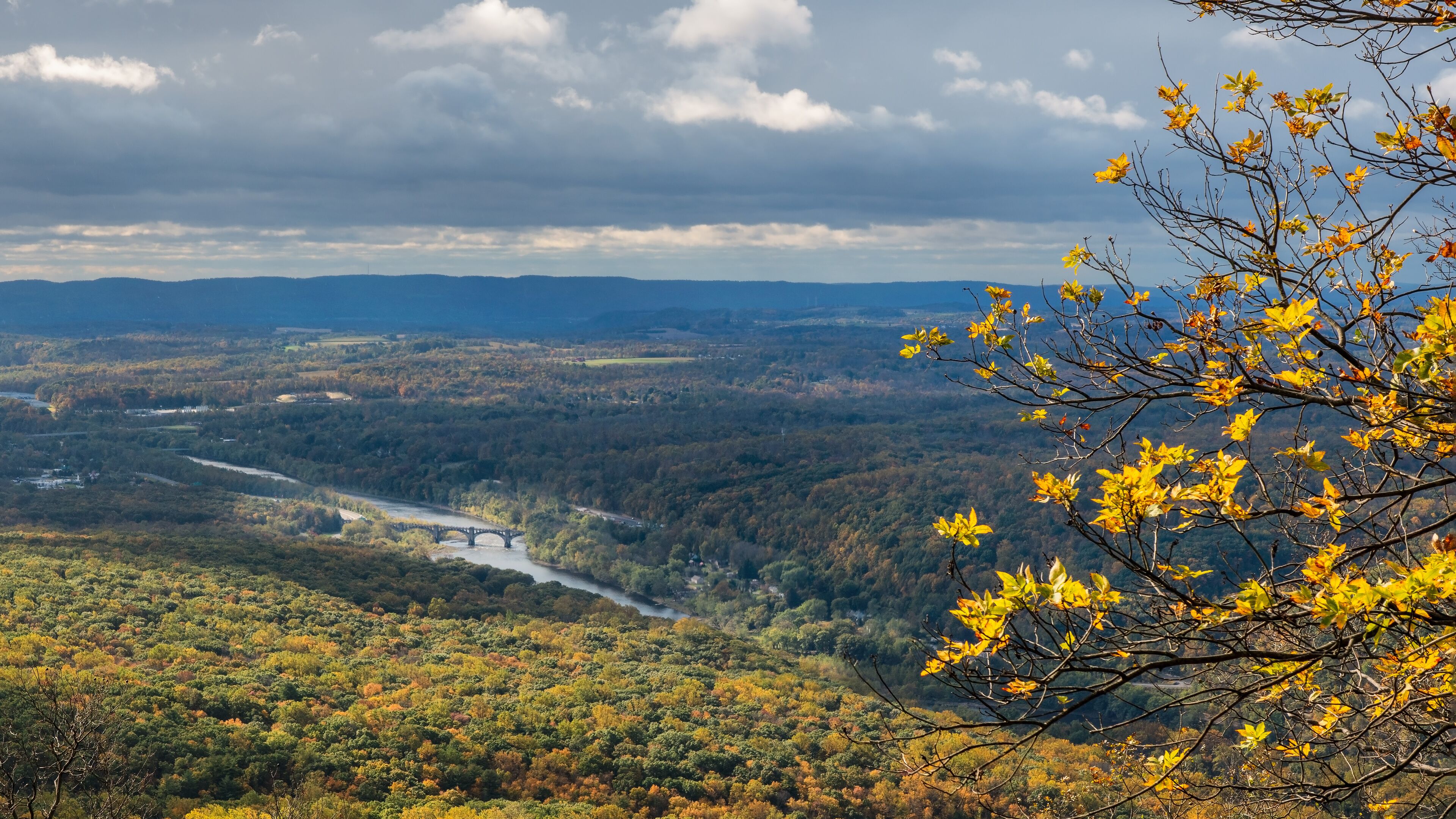 A river flowing through a forested valley with a bridge and autumn foliage.