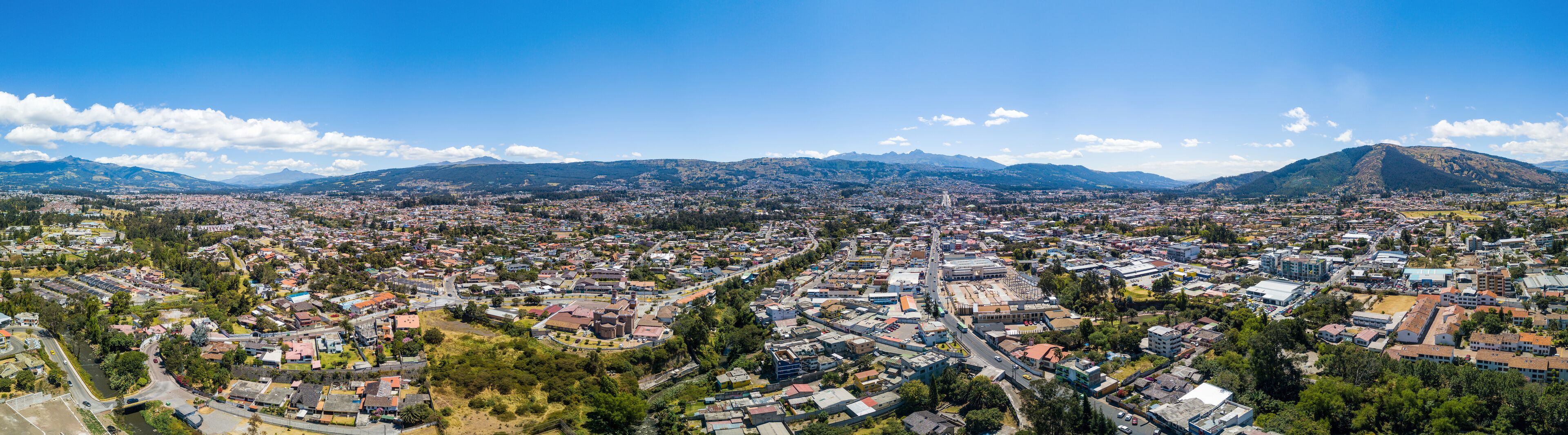 A panoramic view of a city with a river, surrounded by mountains and greenery.