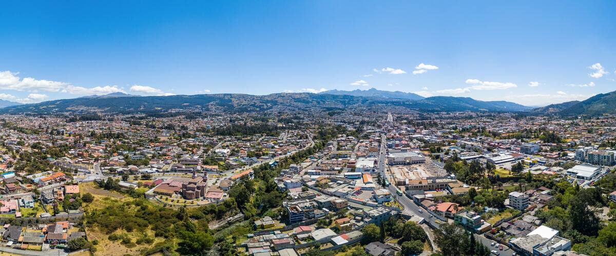 A panoramic view of a city with a river, surrounded by mountains and greenery.