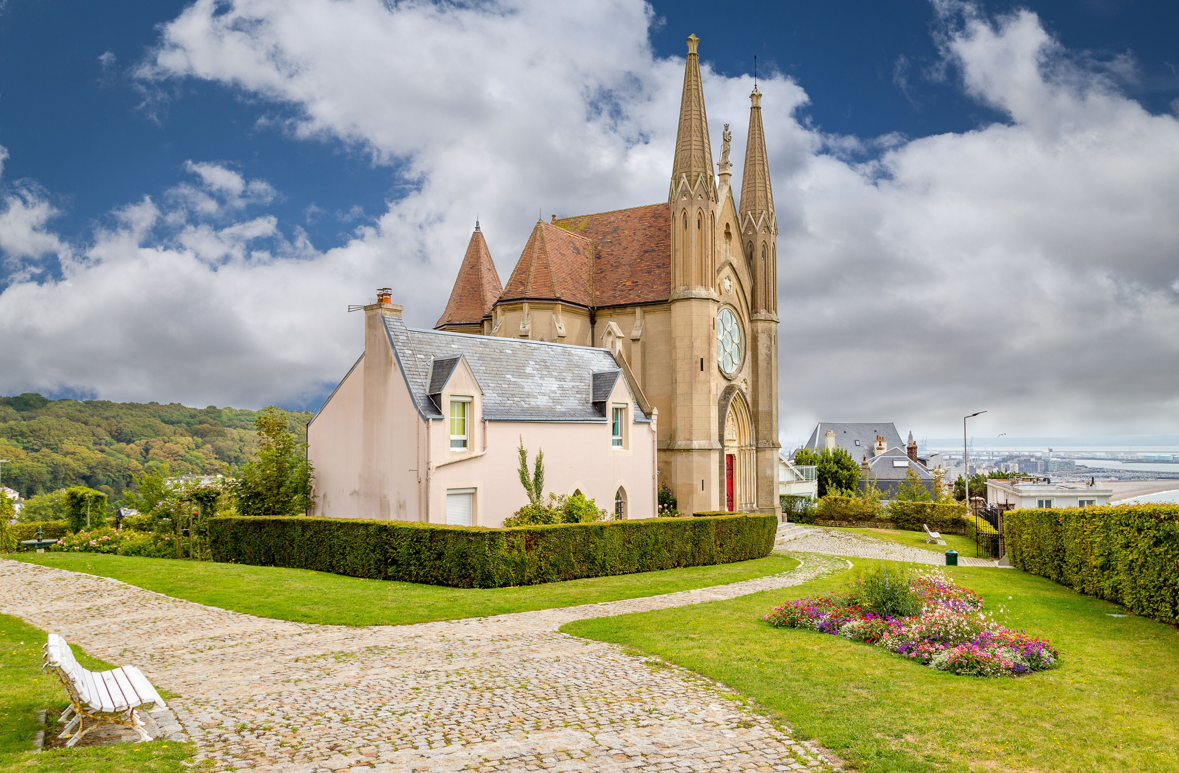 A church with a clock tower, a cobblestone path, and a bench.
