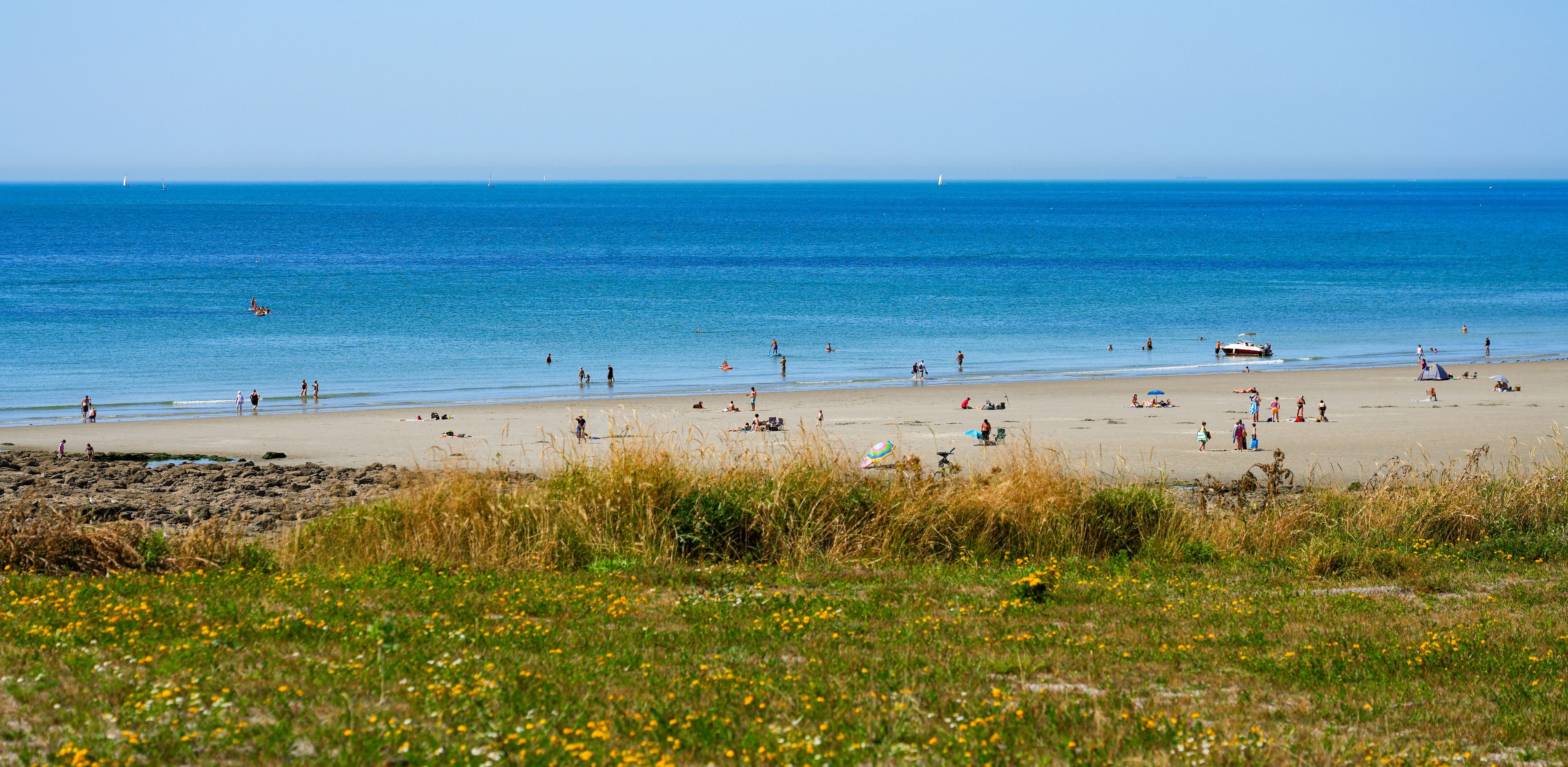 A beach with people, boats, and a clear blue sky.