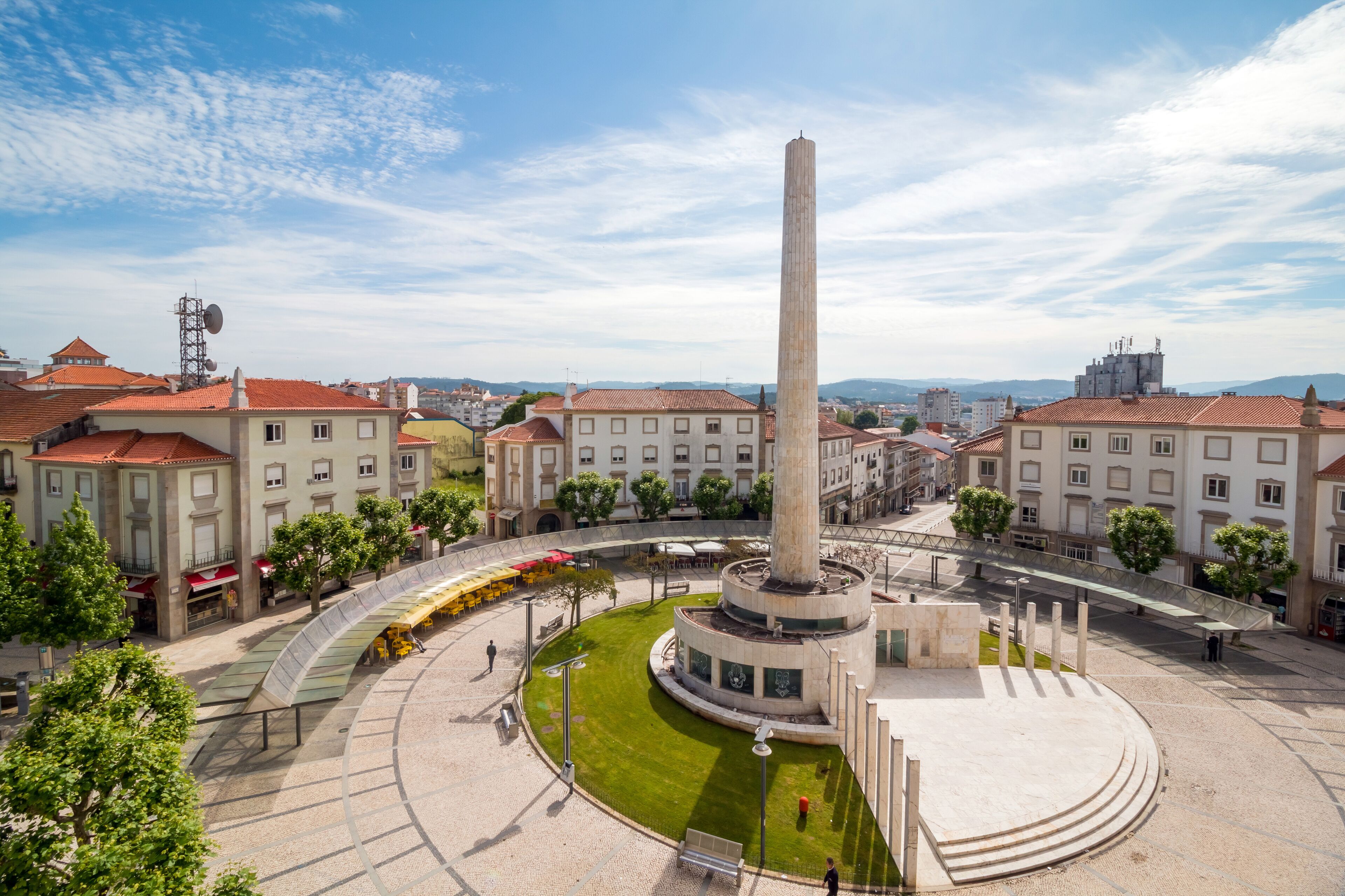 A plaza with a central monument, surrounded by buildings with red-tiled roofs.