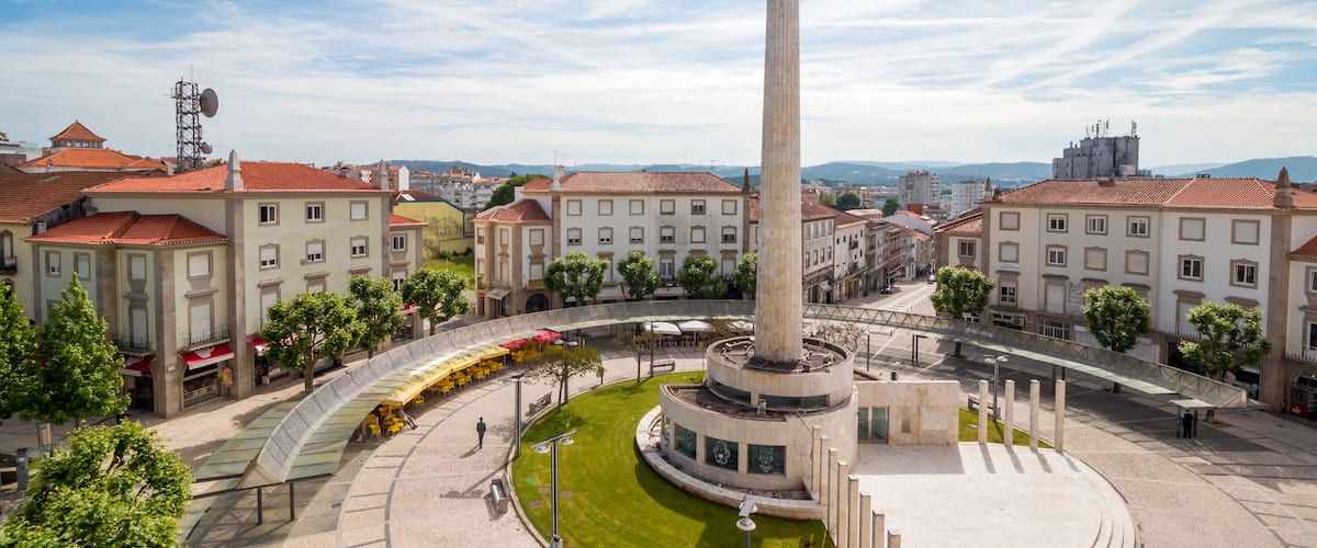A plaza with a central monument, surrounded by buildings with red-tiled roofs.