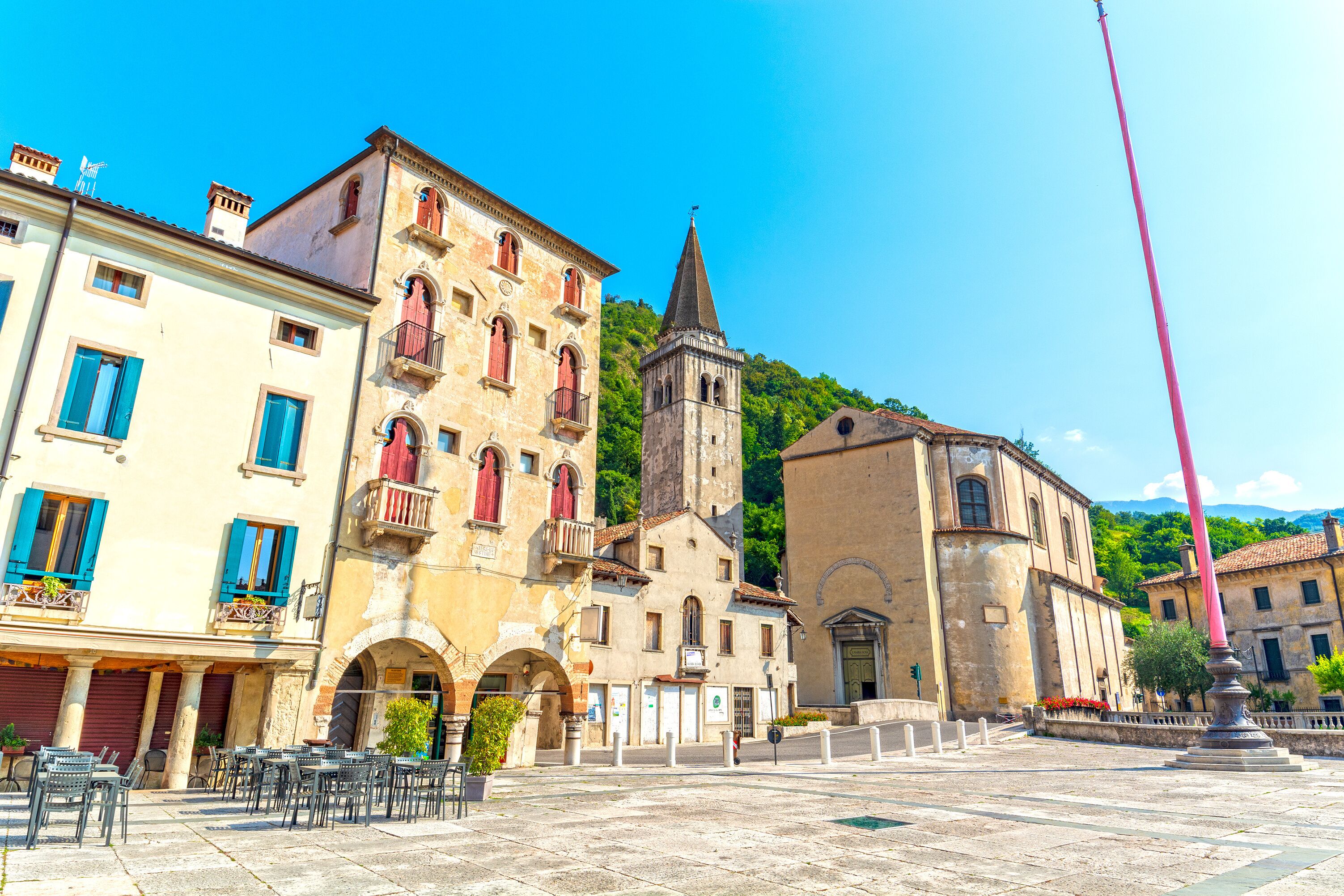 A historic town square with a church tower, traditional buildings, and outdoor seating.