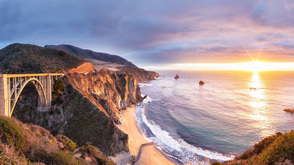 A coastal bridge with a sunset in the background.