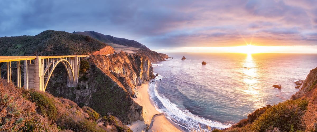 A coastal bridge with a sunset in the background.