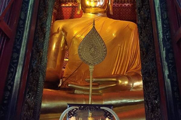 A large golden Buddha statue in a temple with intricate carvings and a red interior.