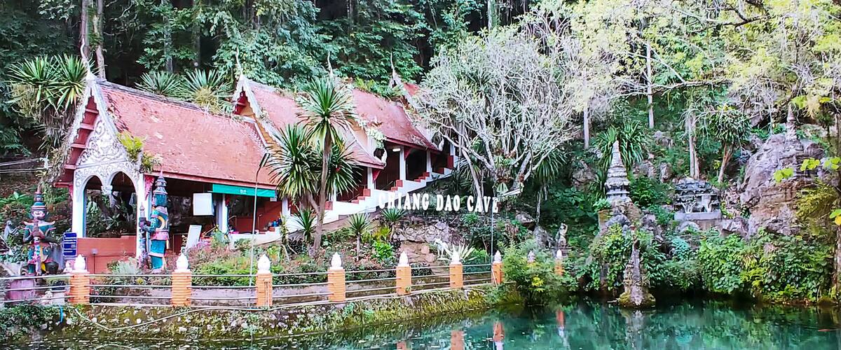 A traditional Thai building with a red roof, surrounded by lush greenery and a calm water body.