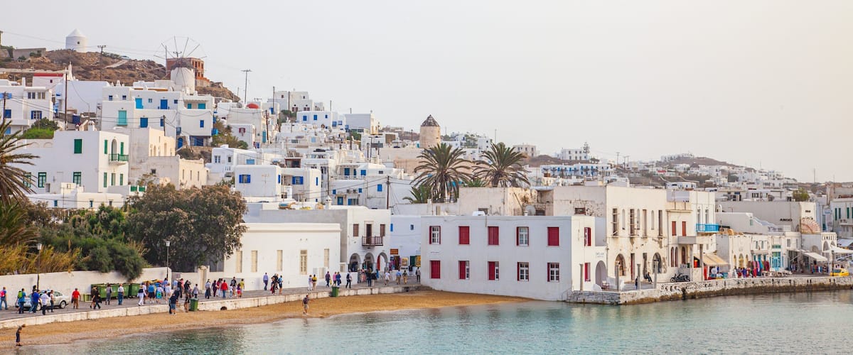 A coastal town with white buildings, a windmill, and a beach with people.