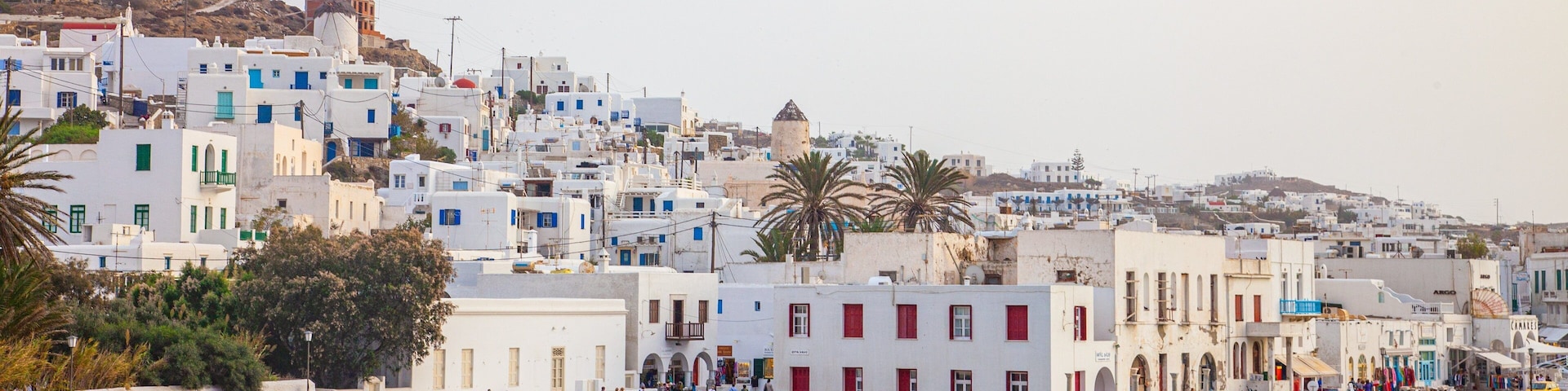 A coastal town with white buildings, a windmill, and a beach with people.