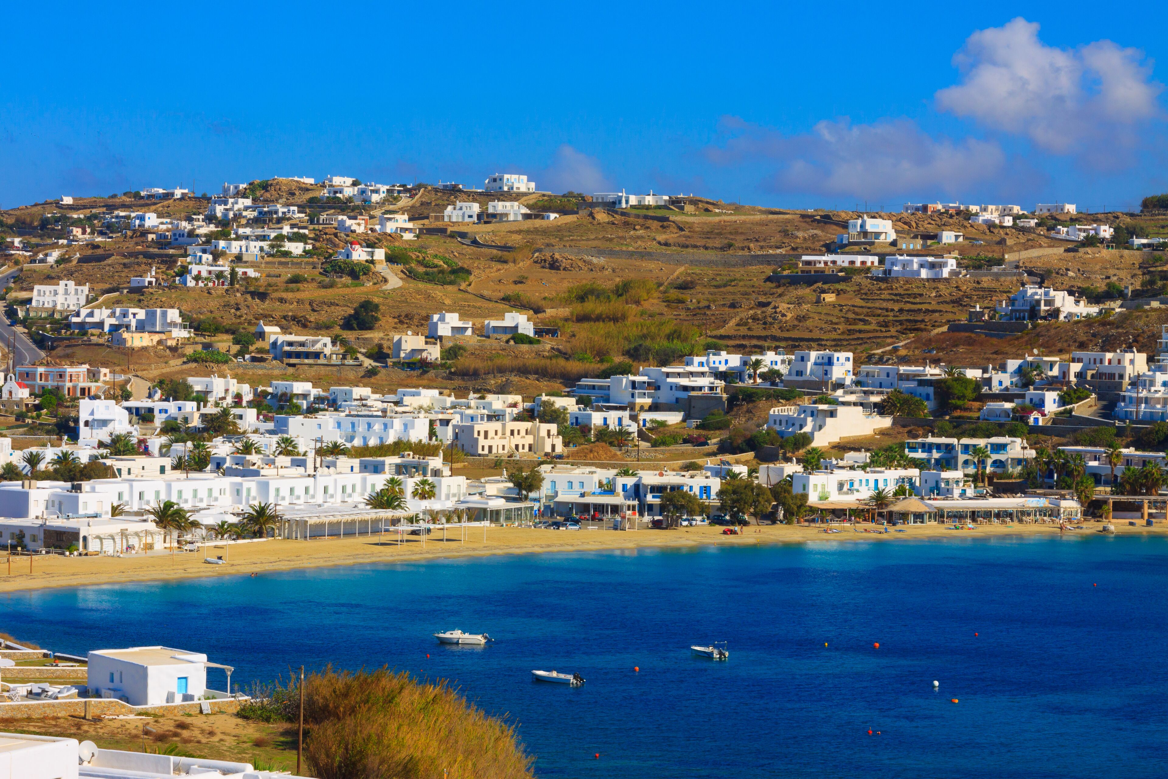 A coastal town with white buildings, a beach, and boats on the water.